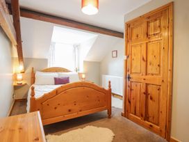 A bedroom with a wooden bed frame two bedside tables with lamps a wooden door and exposed ceiling beams at Llys-y-Wennol in Penmachno