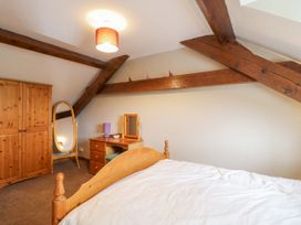 A bedroom with wooden bed frame wardrobe dressing table and mirror with exposed wooden ceiling beams at Llys-y-Wennol in Penmachno