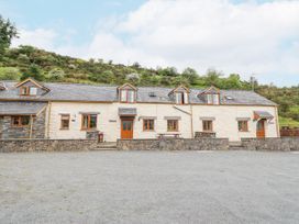 A stone and plaster house with wooden windows and doors set against a hillside at Llys-y-Wennol in Penmachno