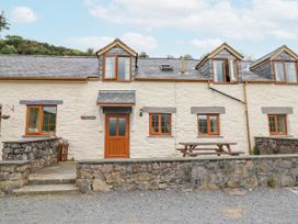 A row of stone cottages with wooden doors and windows and a picnic table outside at Llys-y-Wennol in Penmachno