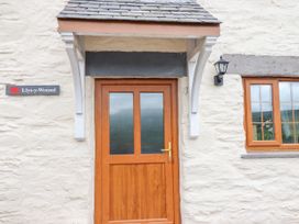 A wooden door with glass panels under a small roof and a window on a stone wall at Llys-y-Wennol in Penmachno