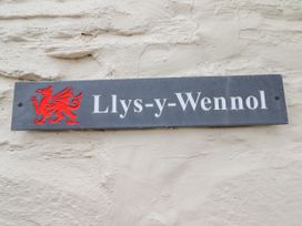 A sign with a red dragon and the text Llys-y-Wennol on a textured wall at Llys-y-Wennol in Penmachno