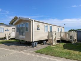 A beige mobile home with a deck and steps on a paved and grassy area at Seabreeze Cottage in East Wittering
