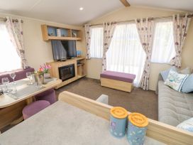 A living room with a television on a wooden stand with a fireplace below and a dining table with glasses and a wine bucket at Seabreeze Cottage in East Wittering