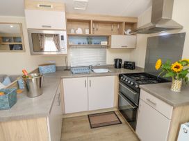 A kitchen with a microwave oven a stove sink and flowers on the counter at Seabreeze Cottage in East Wittering
