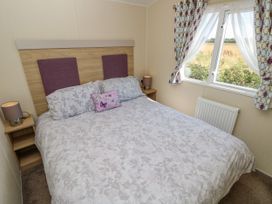 A bedroom with a double bed with floral bedding bedside tables with lamps and a window with patterned curtains at Seabreeze Cottage in East Wittering