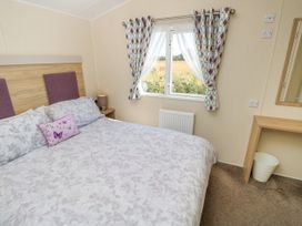 A bedroom with a bed a bedside table with a lamp patterned curtains a window and a desk with a mirror at Seabreeze Cottage in East Wittering