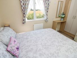 A bedroom with a double bed a window with patterned curtains a wooden dressing table with a mirror and a bouquet of flowers in a vase at Seabreeze Cottage in East Wittering