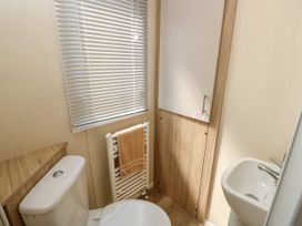 A small bathroom with a toilet, sink, towel radiator with a towel, and a window with blinds at Seabreeze Cottage in East Wittering