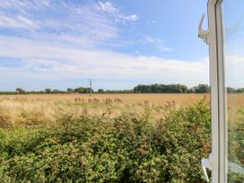 View of a field with bushes in the foreground and trees in the background seen from an open window at Seabreeze Cottage in East Wittering