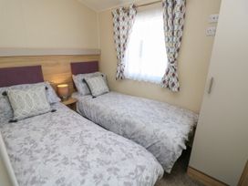 A bedroom with two single beds a nightstand with a lamp a window with curtains and a wardrobe at Seabreeze Cottage in East Wittering