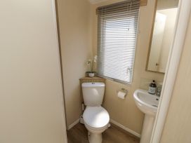 A small bathroom with a toilet a sink a window with blinds and a small plant on a corner shelf at Seabreeze Cottage in East Wittering