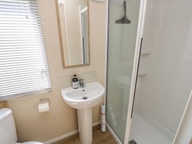 A bathroom with a toilet, a pedestal sink with soap, a mirror, a shower enclosure, and window blinds at Seabreeze Cottage in East Wittering