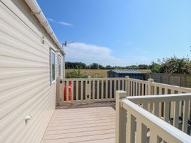 A deck area with beige railings attached to a beige mobile home with fields and a shed in the background at Seabreeze Cottage in East Wittering