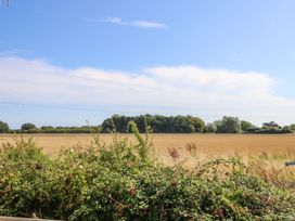 An open field with shrubs in the foreground and trees in the background under a blue sky at Seabreeze Cottage in East Wittering
