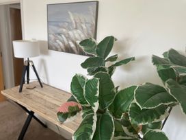 A living room with a table, lamp, plant, and painting at Plas Darien Apartment 7 in Trearddur Bay