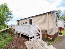 A beige mobile home with a white railing veranda and steps next to a wooden table with a plant pot at 25 Manleigh Park in Combe Martin