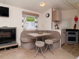 A small dining area with a corner bench sofa table and two stools next to a kitchen with an oven and a wall clock at 26 Manleigh Park in Combe Martin