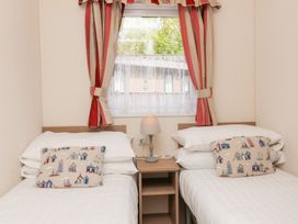 A bedroom with two single beds a nightstand with a lamp and a window with striped curtains at 26 Manleigh Park Combe Martin