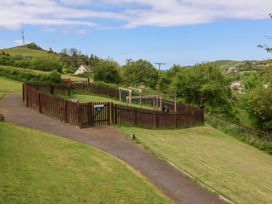 A fenced playground with climbing equipment and a gate on a grassy hill at 26 Manleigh Park in Combe Martin