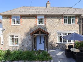 Exterior of a stone house with white-framed windows a wooden porch door a garden bed and outdoor seating with an umbrella at Myrtle Cottage in Uplyme