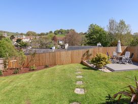 A garden with a grass lawn a wooden fence a patio table with chairs and an umbrella at Myrtle Cottage in Uplyme
