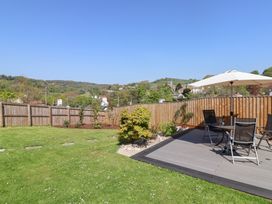 A garden with a lawn and a patio with table umbrella and chairs at Myrtle Cottage in Uplyme