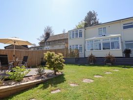 A garden with lawn chairs table and umbrella next to a patio and a two story house with a conservatory at Myrtle Cottage in Uplyme