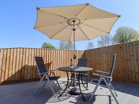 An outdoor patio with a round table under a large umbrella surrounded by three chairs and a wooden fence