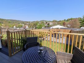 A balcony with a round table and two chairs overlooking a garden with a fenced seating area and hills in the background at Myrtle Cottage in Uplyme