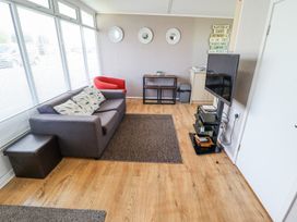 A living room with a gray sofa red chair wall art and a mounted television at 68 Cherry Park in Chapel St Leonards