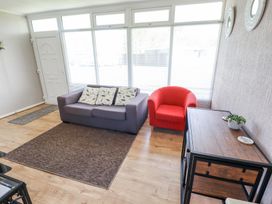 A living room with a gray sofa with three pillows a red armchair a wooden cabinet with a plant and coasters on top and large windows at 68 Cherry Park in Chapel St Leonards