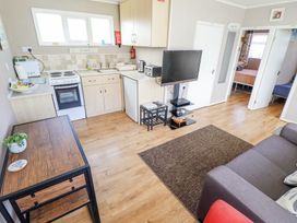 A small kitchen area with stove and refrigerator next to a living room with a couch and TV at 68 Cherry Park in Chapel St Leonards
