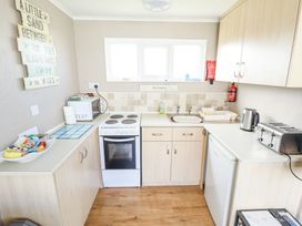 A small kitchen with stove microwave kettle toaster and sink at 68 Cherry Park in Chapel St Leonards