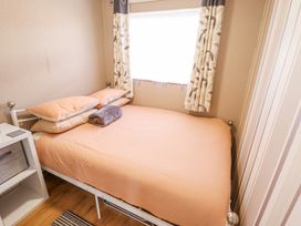 A small bedroom with a bed covered in peach bedding and pillows next to a window with leaf patterned curtains at 68 Cherry Park Chapel St Leonards