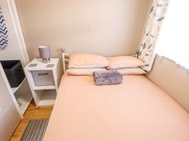 A bedroom with a double bed with pillows and a blanket a bedside table with a lamp and a storage basket at 68 Cherry Park in Chapel St Leonards