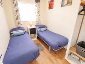A bedroom with two single beds a small table with a lamp between the beds and an open closet at 68 Cherry Park in Chapel St Leonards
