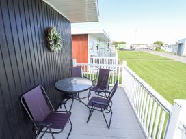 A balcony with a round glass table and four chairs overlooking a lawn at 68 Cherry Park in Chapel St Leonards