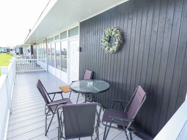 An outdoor patio with a round glass table and four chairs near a white door with a floral wreath on the black wooden wall at 68 Cherry Park in Chapel St Leonards