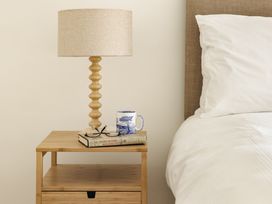 A bedroom with a nightstand, lamp, mug, book, and eyeglasses at Tethers End in Lindeth near Bowness-On-Windermere