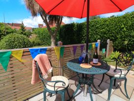 A patio table with two chairs under a red umbrella with a bottle and glasses on the table at 3 Palms in Preston Sands