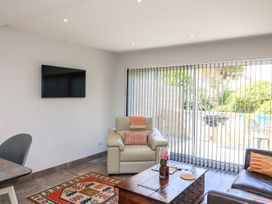 A living room with a wall-mounted TV an armchair a wooden coffee table and vertical blinds at 3 Palms in Preston Sands