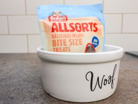 A white ceramic bowl with the word Woof on the side containing a pack of Bakers Allsorts bite size treats on a kitchen counter