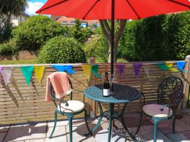 A patio set with two chairs and a table under a red umbrella with a bottle and glasses on it and a garden background at 3 Palms in Preston Sands