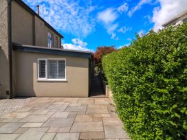 An exterior view of a house with a paved patio area a window with shutters on a wall and a green hedge along a narrow pathway at 3 Palms in Preston Sands