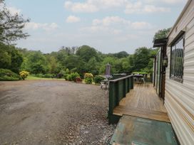 A caravan with a wooden deck and outdoor tables overlooking a gravel area and trees at Lazy Trout Caravan in Ludchurch near Narberth