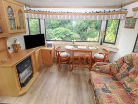 A living room with wooden cabinets a patterned sofa a glass table with two chairs and a television near windows at Lazy Trout Caravan Ludchurch near Narberth