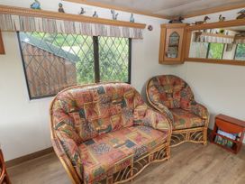 A seating area with patterned cushions on rattan furniture and a window with a valance at Lazy Trout Caravan Ludchurch near Narberth