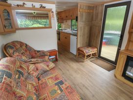 A living area with patterned sofas wooden cabinets a kitchen and a door at Lazy Trout Caravan Ludchurch near Narberth