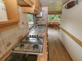 A narrow kitchen with a gas stove, sink, wooden cabinets, and a view of a dining area with a table and chairs through a window at Lazy Trout Caravan Ludchurch near Narberth